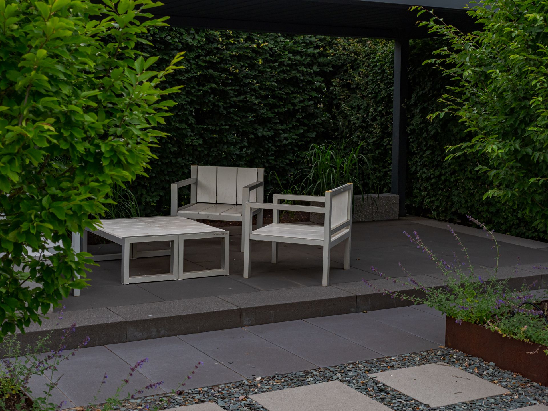 Outdoor chairs and a low table on a stone patio framed by an ivy-covered wall