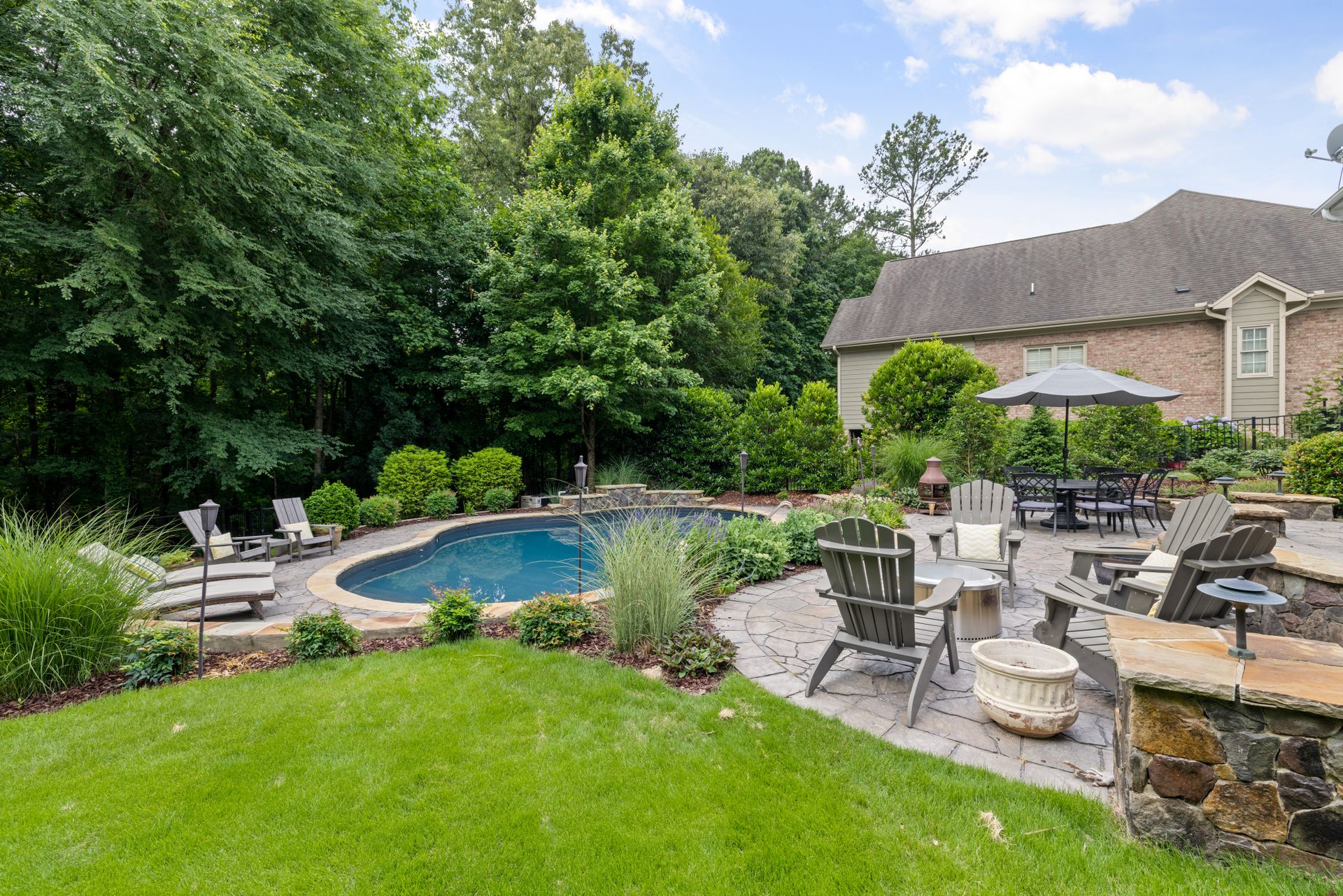A landscaped backyard with a pool, patio and lawn