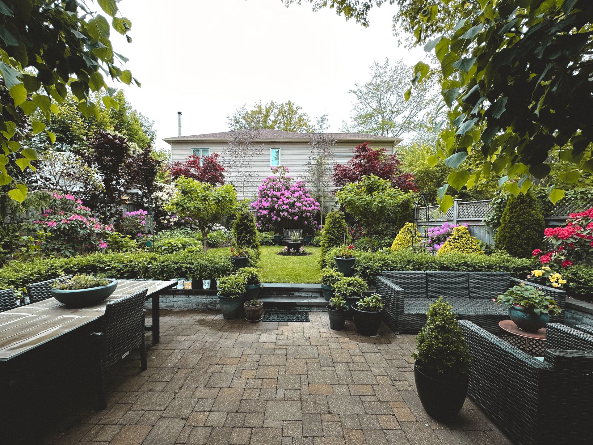 A paver patio with outdoor furniture surrounded by flowering shrubs and beds